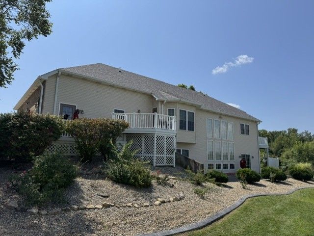 Large beige house with white trim on a sloped landscaped lot under a blue sky