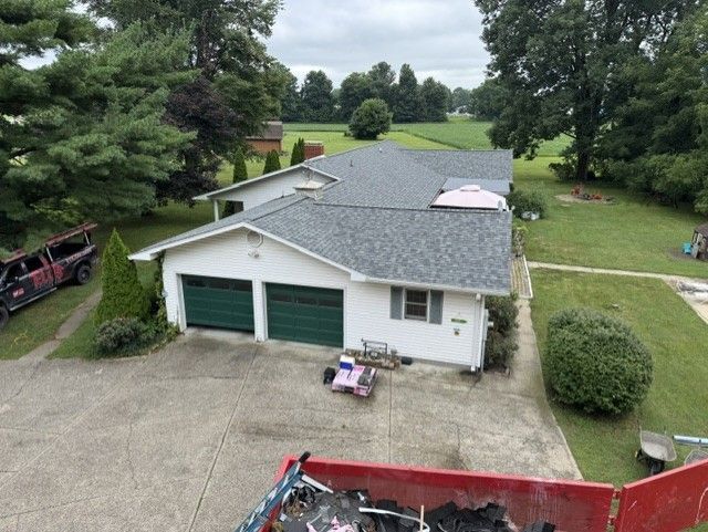 Aerial view of a white garage and house with green doors, surrounded by lawn and trees.