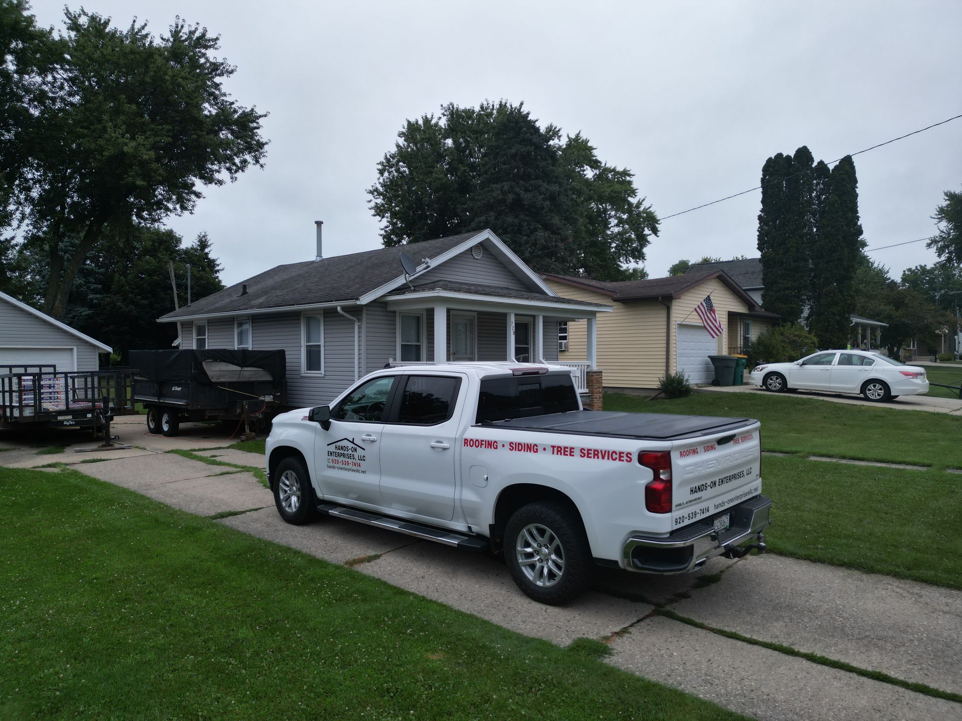 White pickup truck parked in a suburban driveway beside a small house on a cloudy day