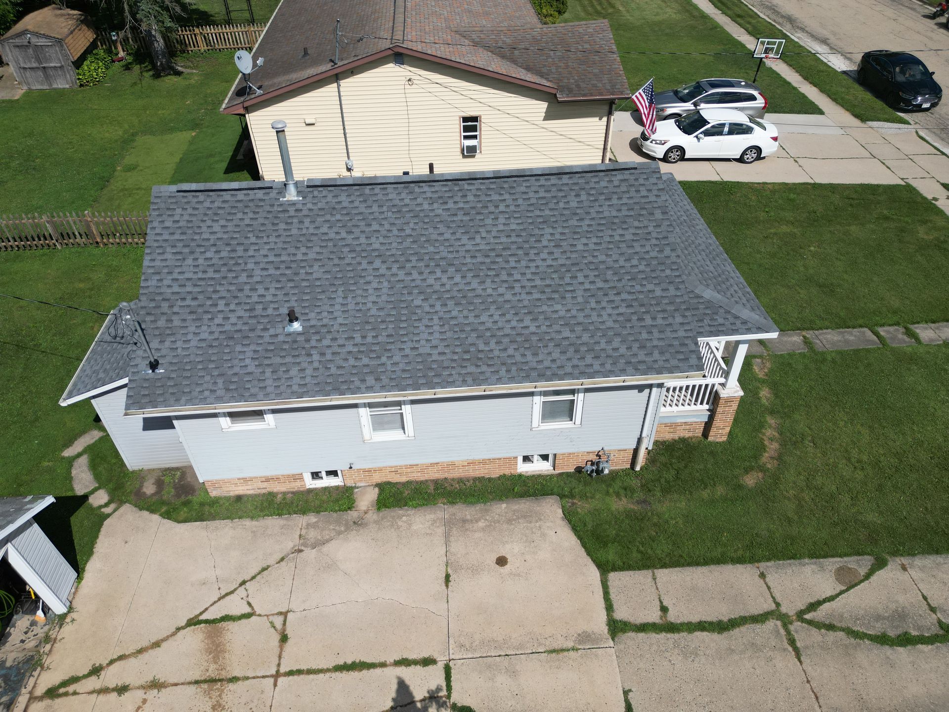 Aerial view of a gray-roofed house with a driveway, lawn, and a parked white SUV nearby.