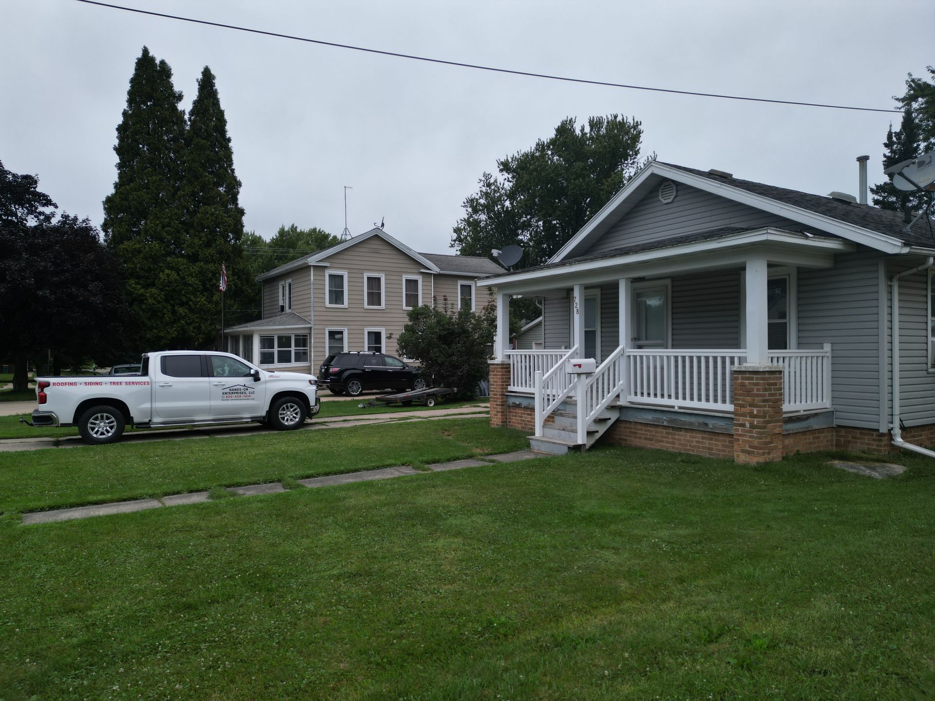 Residential street with a white pickup truck and two houses on a grassy lawn under cloudy skies