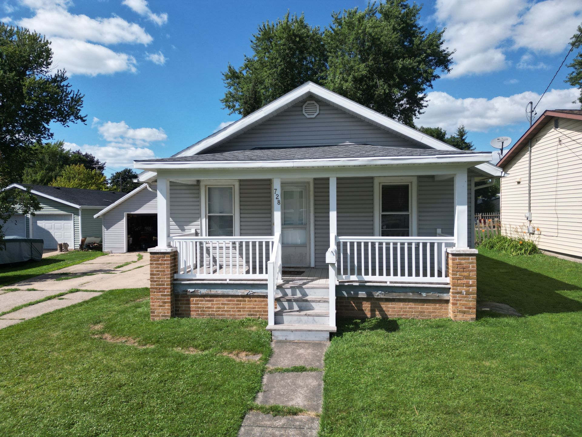 Small gray house with white porch and brick steps on a sunny residential street