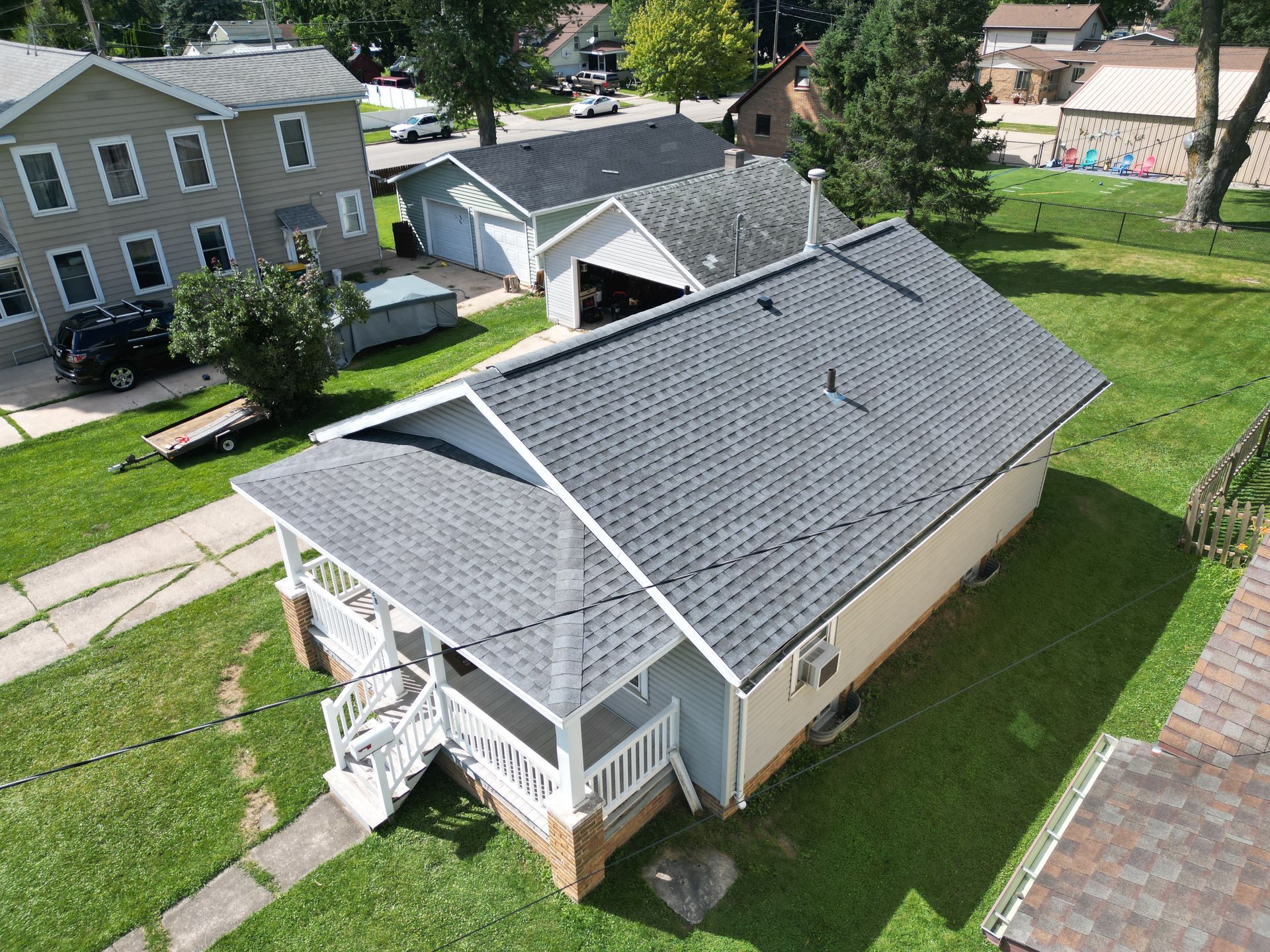 Aerial view of a beige house with a gray roof, porch, and green yard in a residential neighborhood