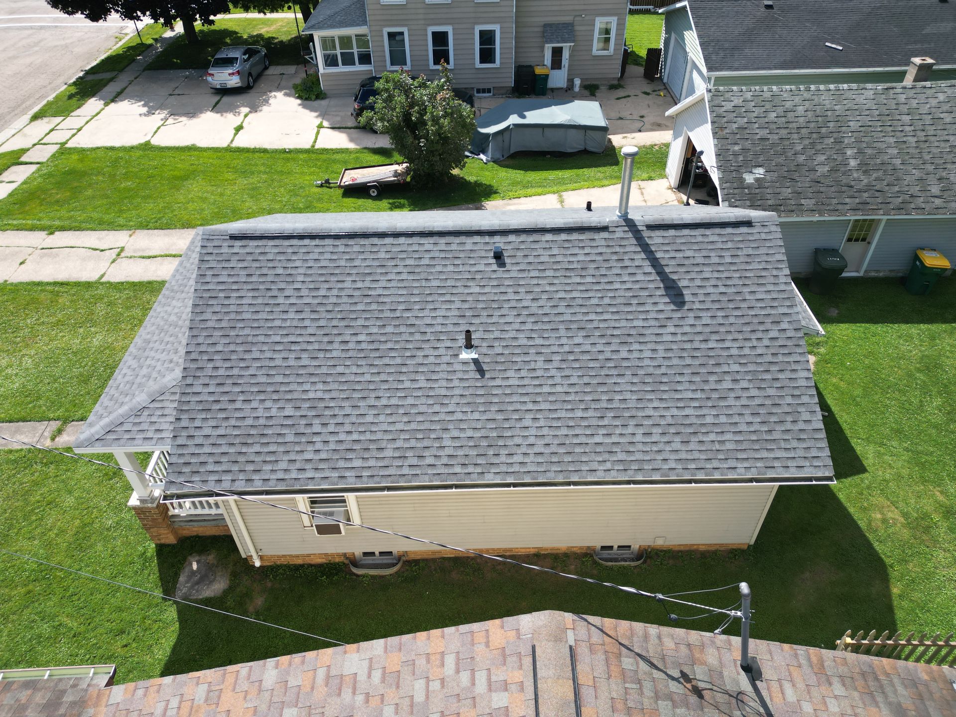 Aerial view of a house with a gray roof, beige walls, and a green backyard in a suburban neighborhood