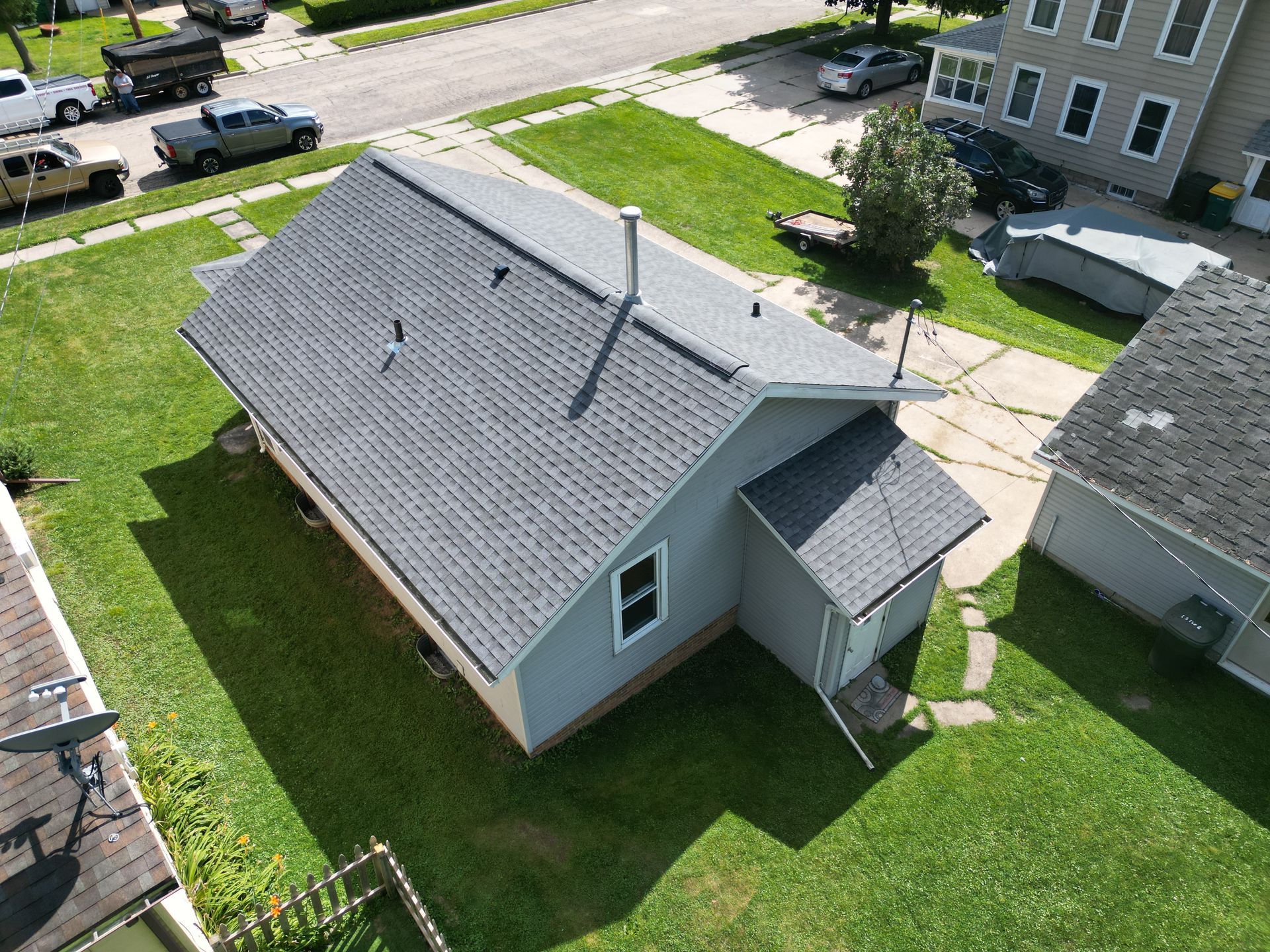 Aerial view of a small gray house with a dark roof and green lawn in a suburban neighborhood.