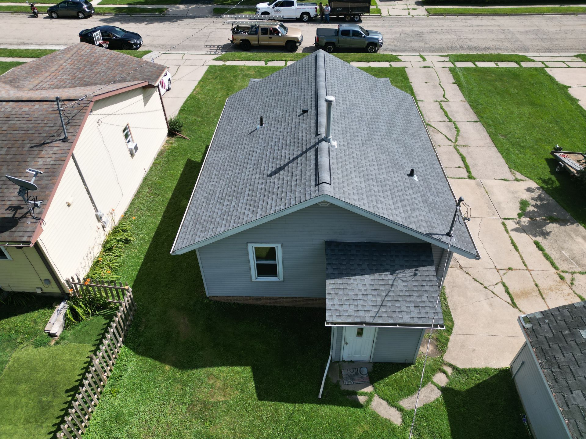 Aerial view of a small gray house with a roof and driveway in a residential neighborhood.