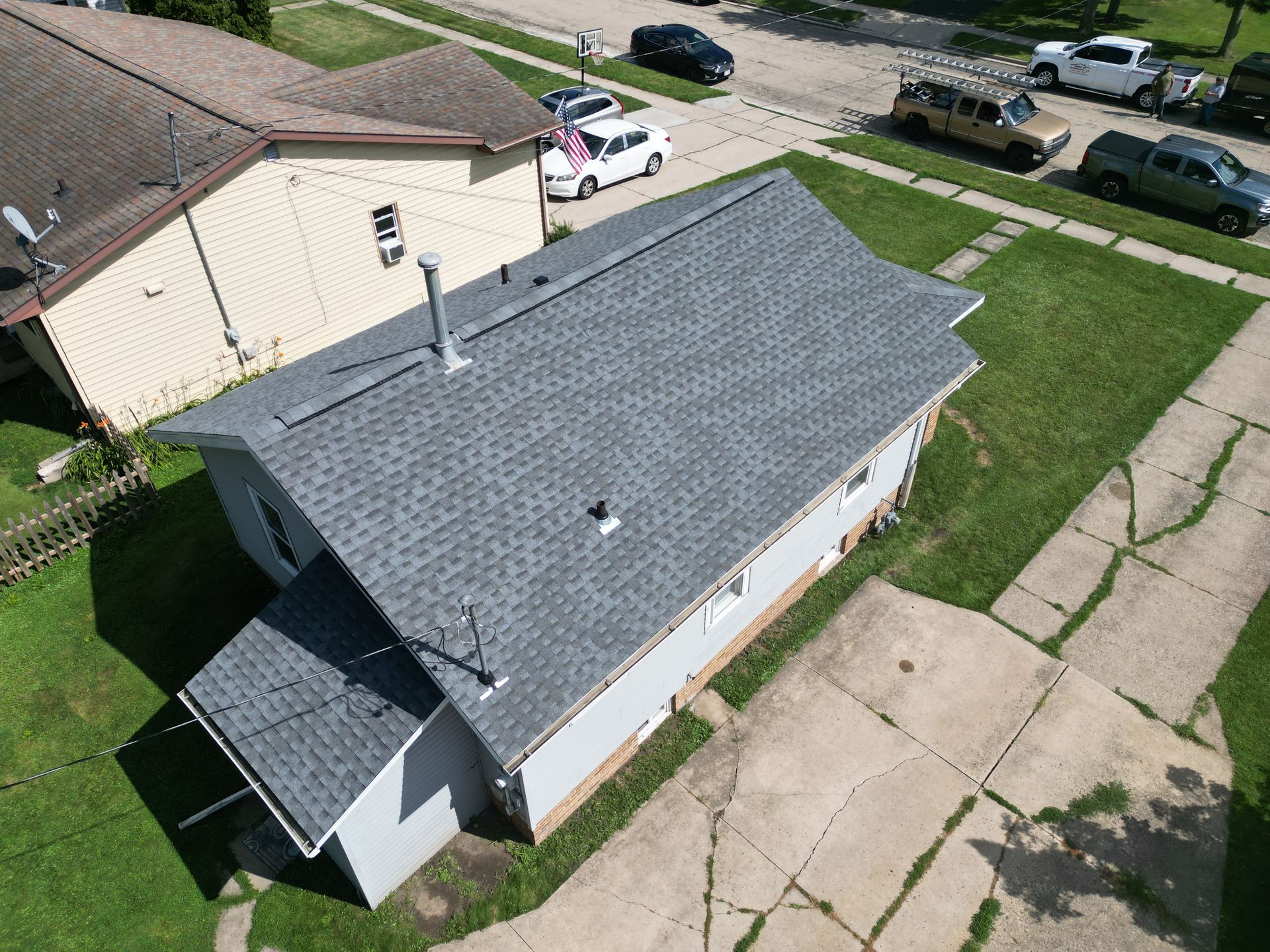 Aerial view of a gray-roofed house with a small porch and driveway in a suburban neighborhood.