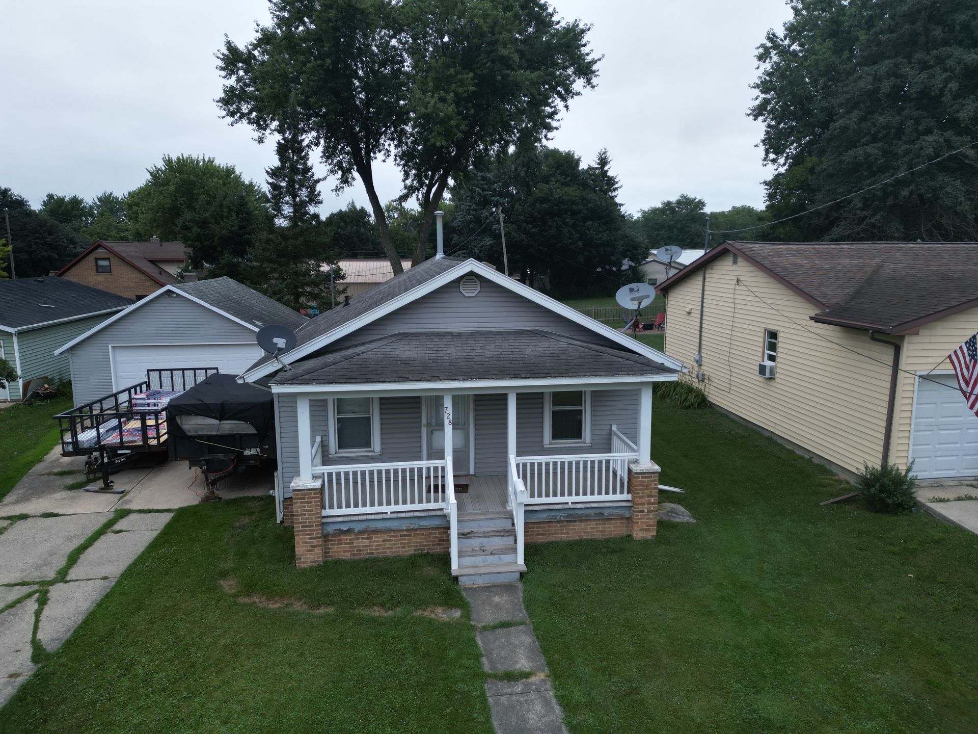 Small gray house with white porch and front walkway in a suburban neighborhood