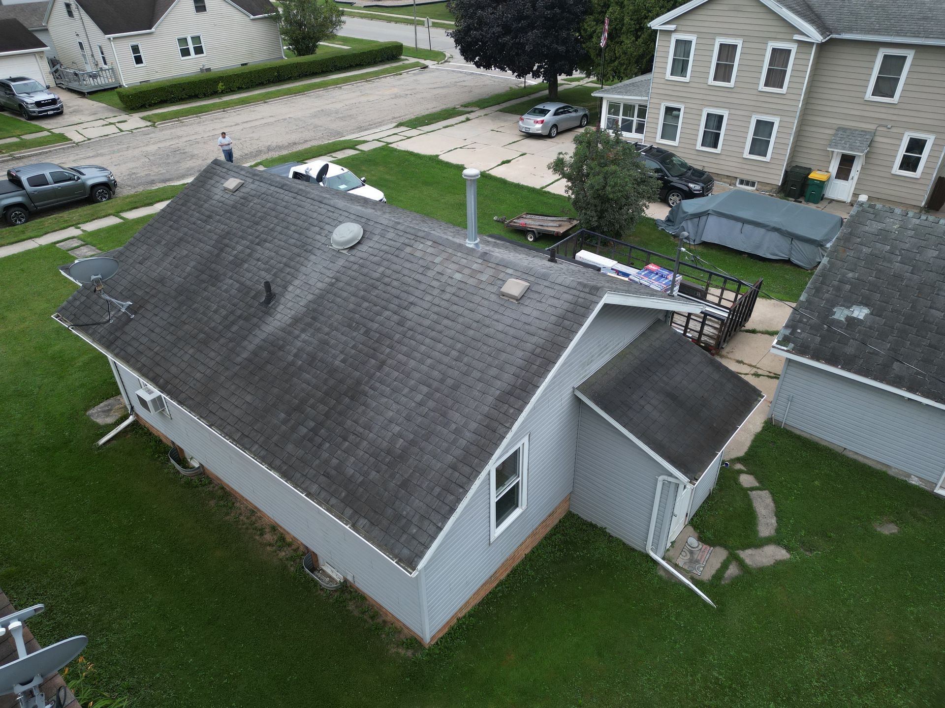 Aerial view of a gray house with a dark roof in a suburban neighborhood, with lawn and neighboring homes.