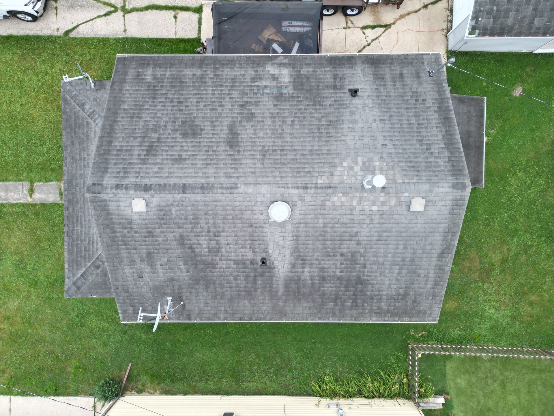 Aerial view of a gray-roofed house surrounded by green grass and neighboring buildings.