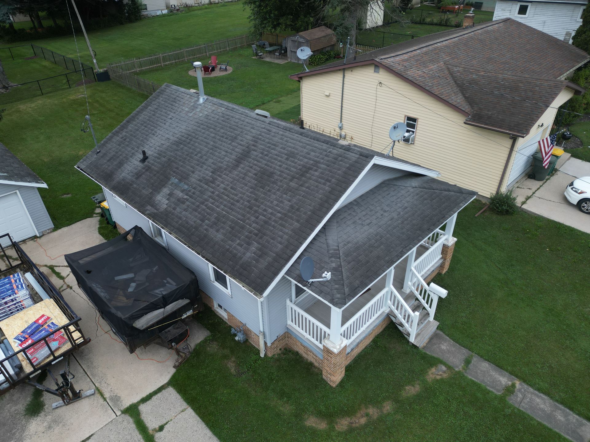 Aerial view of a small house with a black truck in the driveway and a fenced porch beside a beige garage.