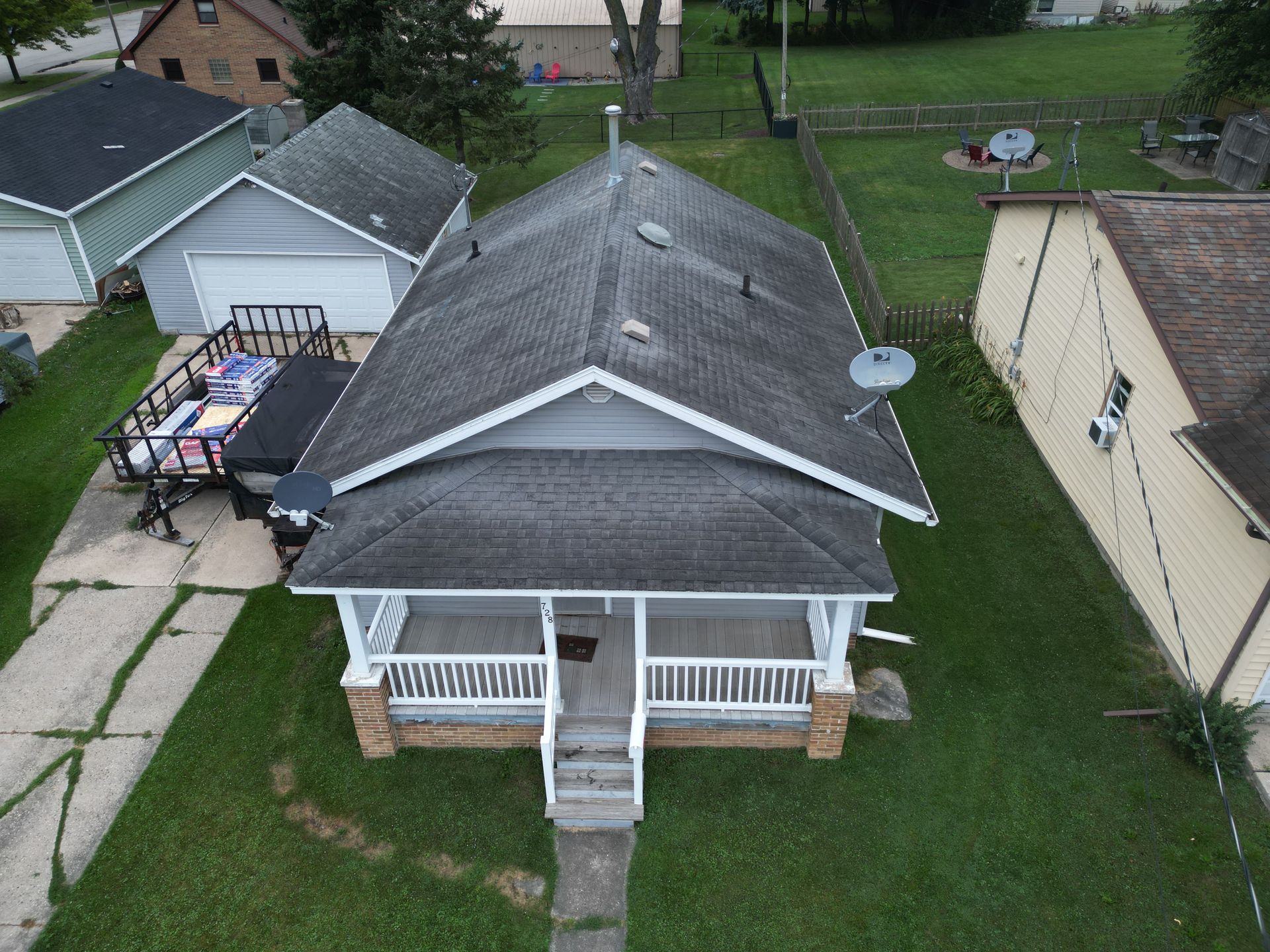 Aerial view of a gray-roofed house with a front porch, driveway, and green yard.