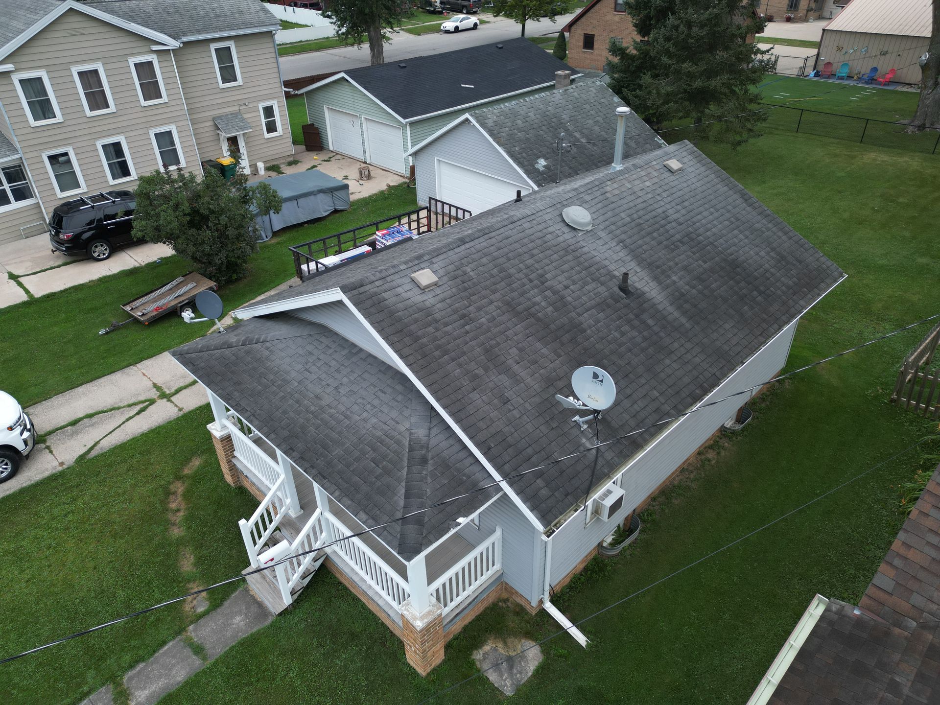 Aerial view of a gray-roofed house with a white porch in a suburban neighborhood.
