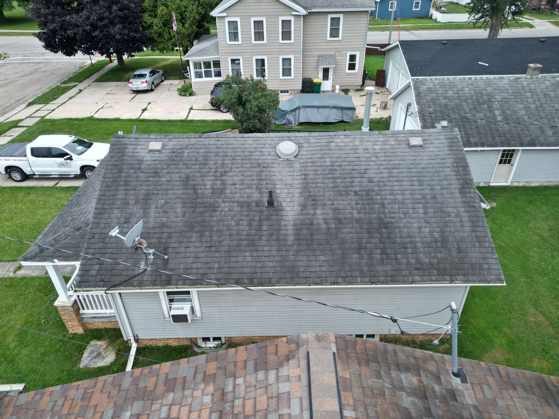 Aerial view of a gray-roofed house with a driveway, lawn, and neighboring homes.