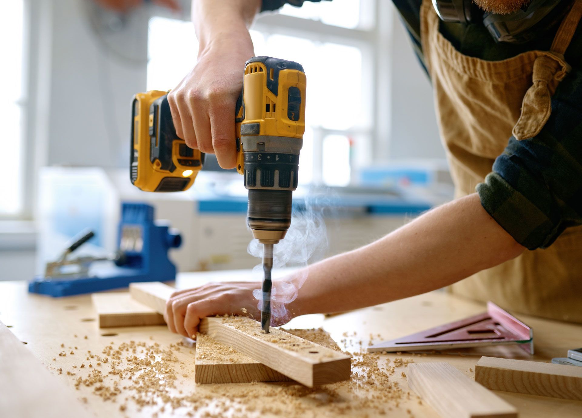 Person drilling wood with a yellow power drill in a bright workshop, wood shavings scattered around.
