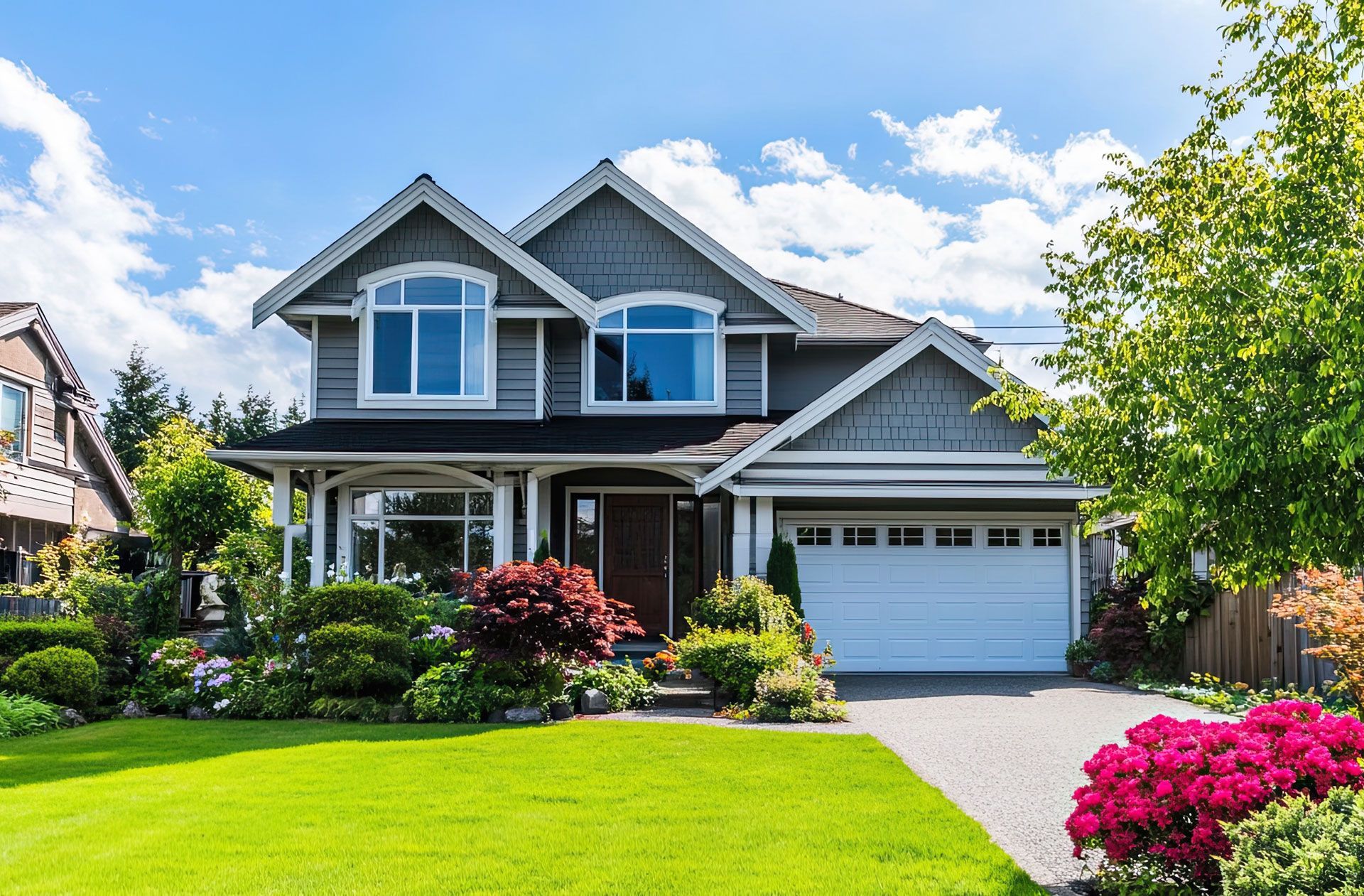 Suburban two-story gray house with white trim, front porch, garage, and bright green lawn under a blue sky