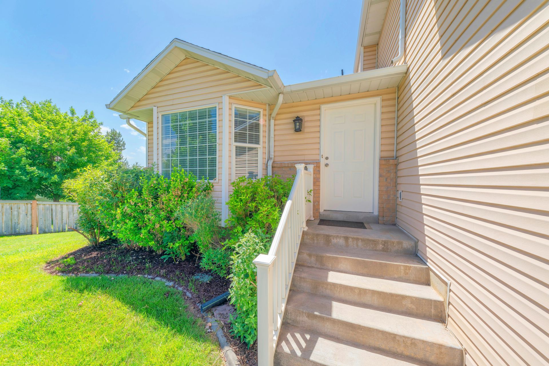 Front entrance of a beige house with white trim, stairs, porch, and green lawn