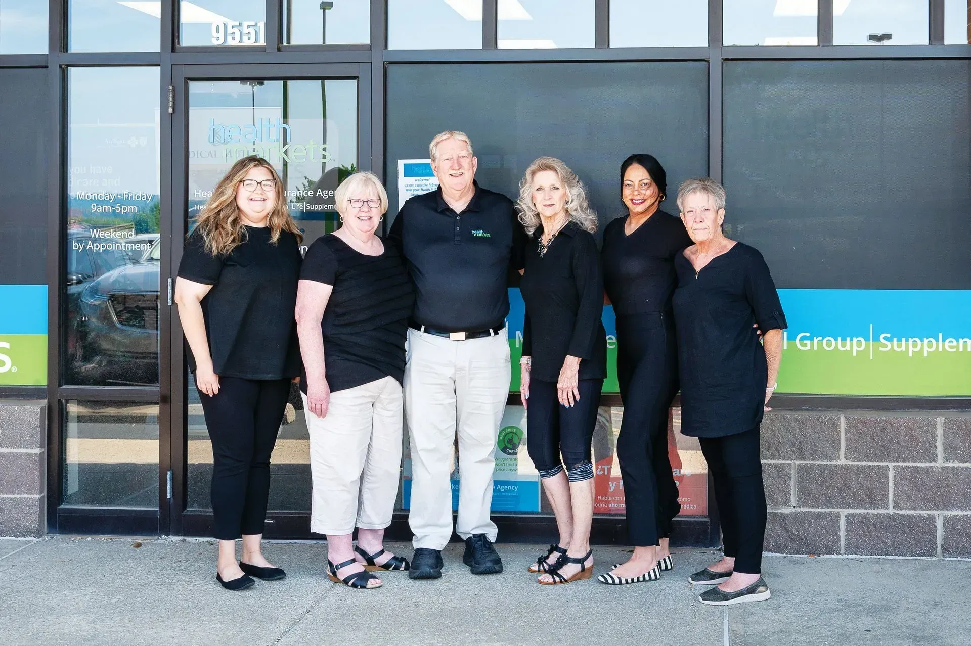 Group of seven people standing in front of a storefront with blue and green accents.