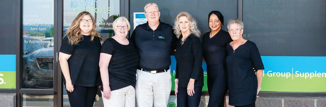 A group of seven people pose outside a building, all wearing dark tops and various bottoms, smiling.