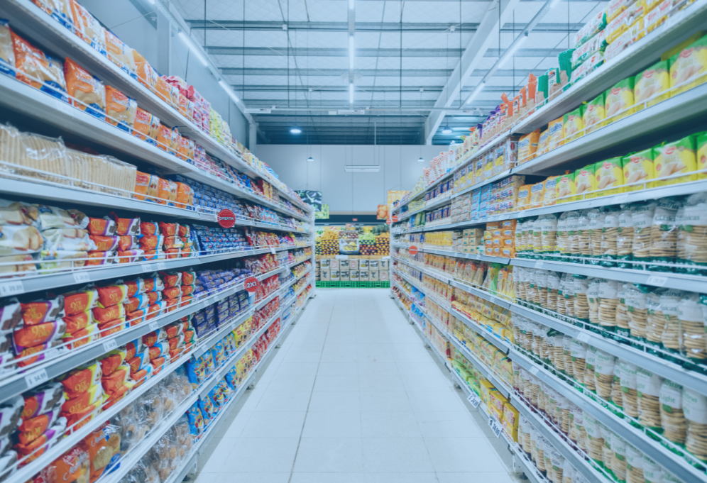 Fileiras de prateleiras de supermercado repletas de produtos alimentícios, bem iluminadas.
