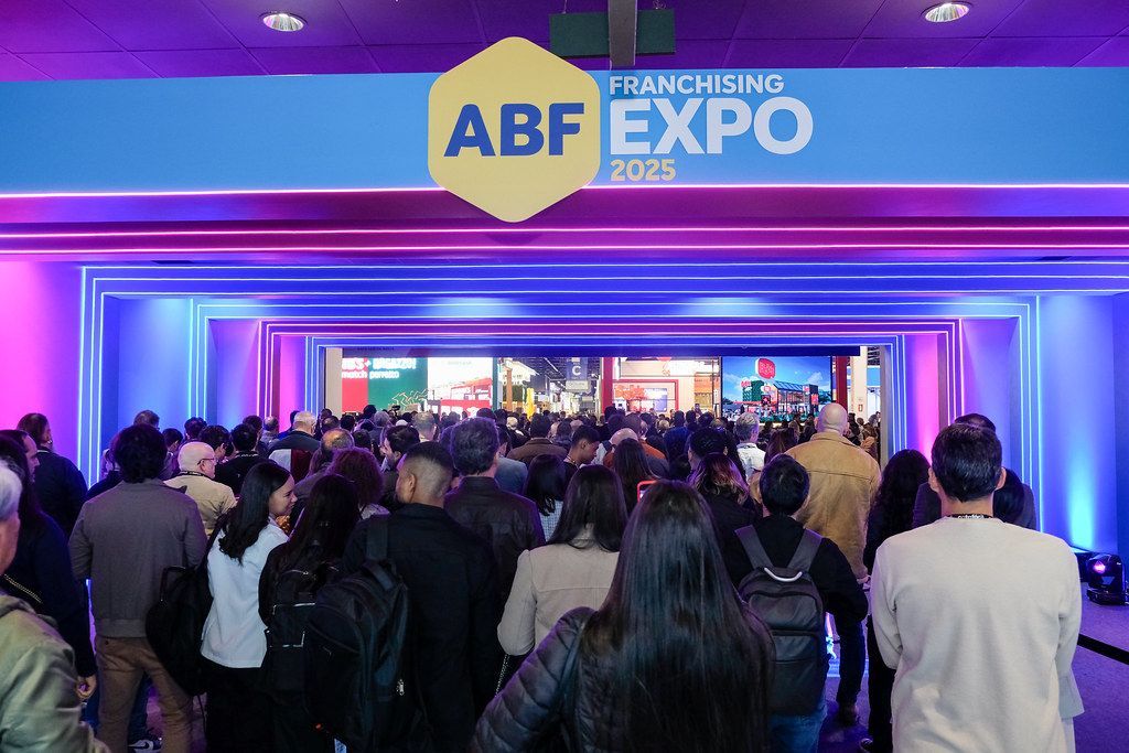 Multidão entrando na ABF Franchising Expo 2025. Iluminação azul e rosa, sinalização e muita gente.