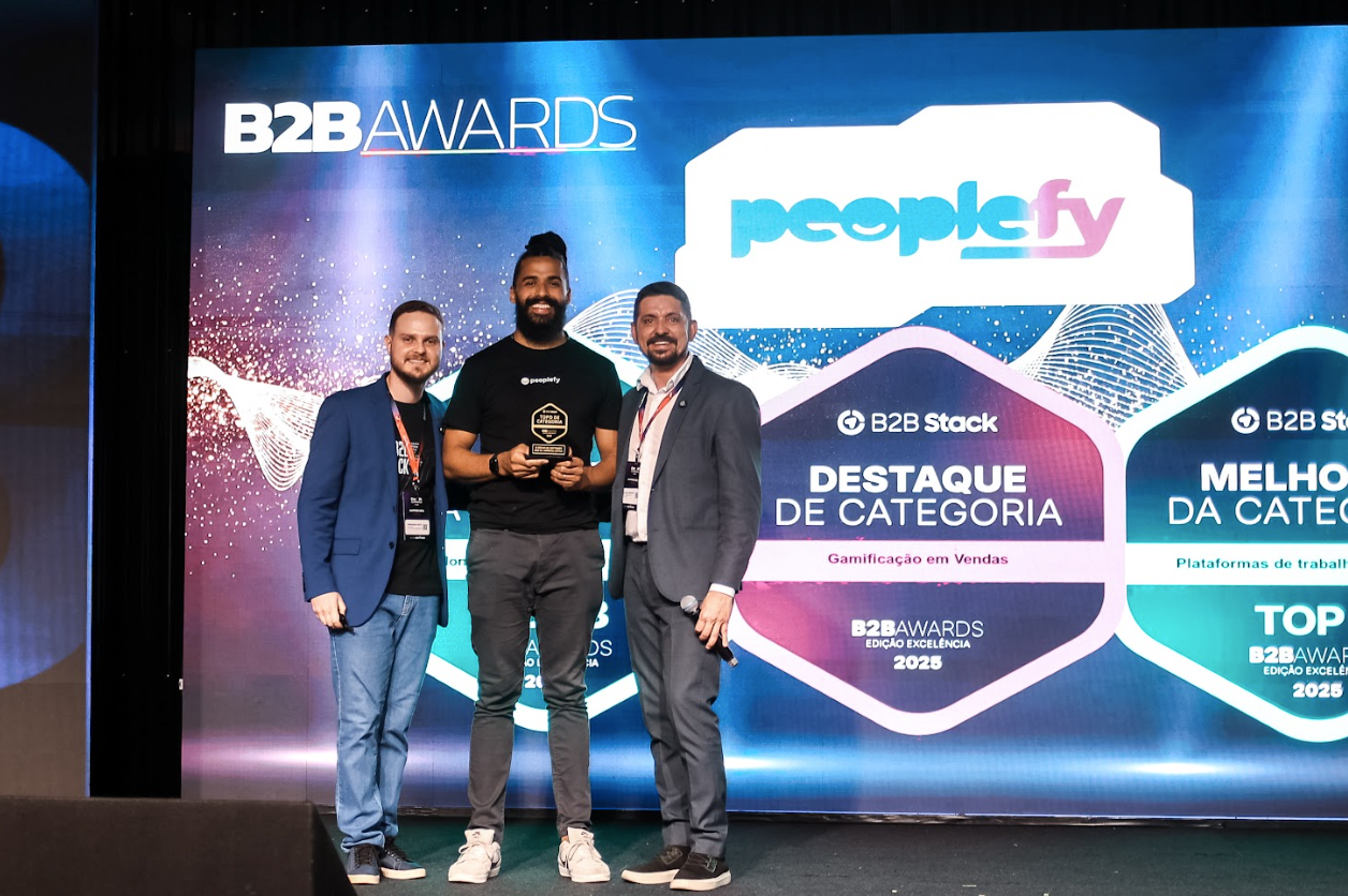 Três pessoas segurando um prêmio na cerimônia de entrega dos B2B Awards. Elas estão em pé em frente a um painel com logotipos.