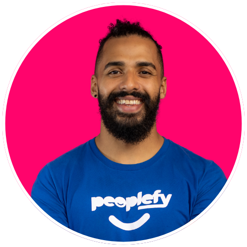 Homem sorridente com barba, vestindo camiseta azul com o logotipo