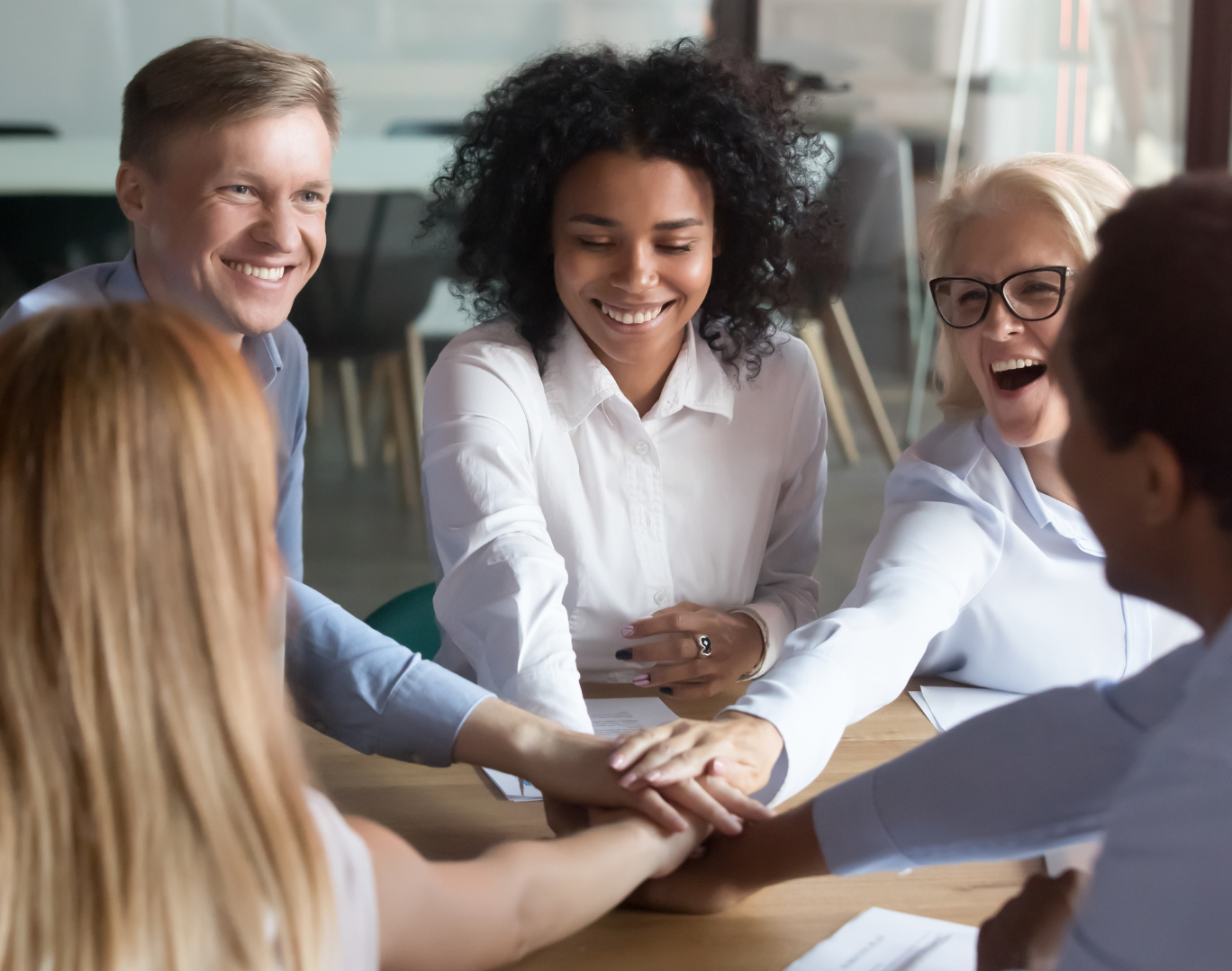 Equipe diversificada de pessoas com as mãos empilhadas, sorrindo, em um escritório.