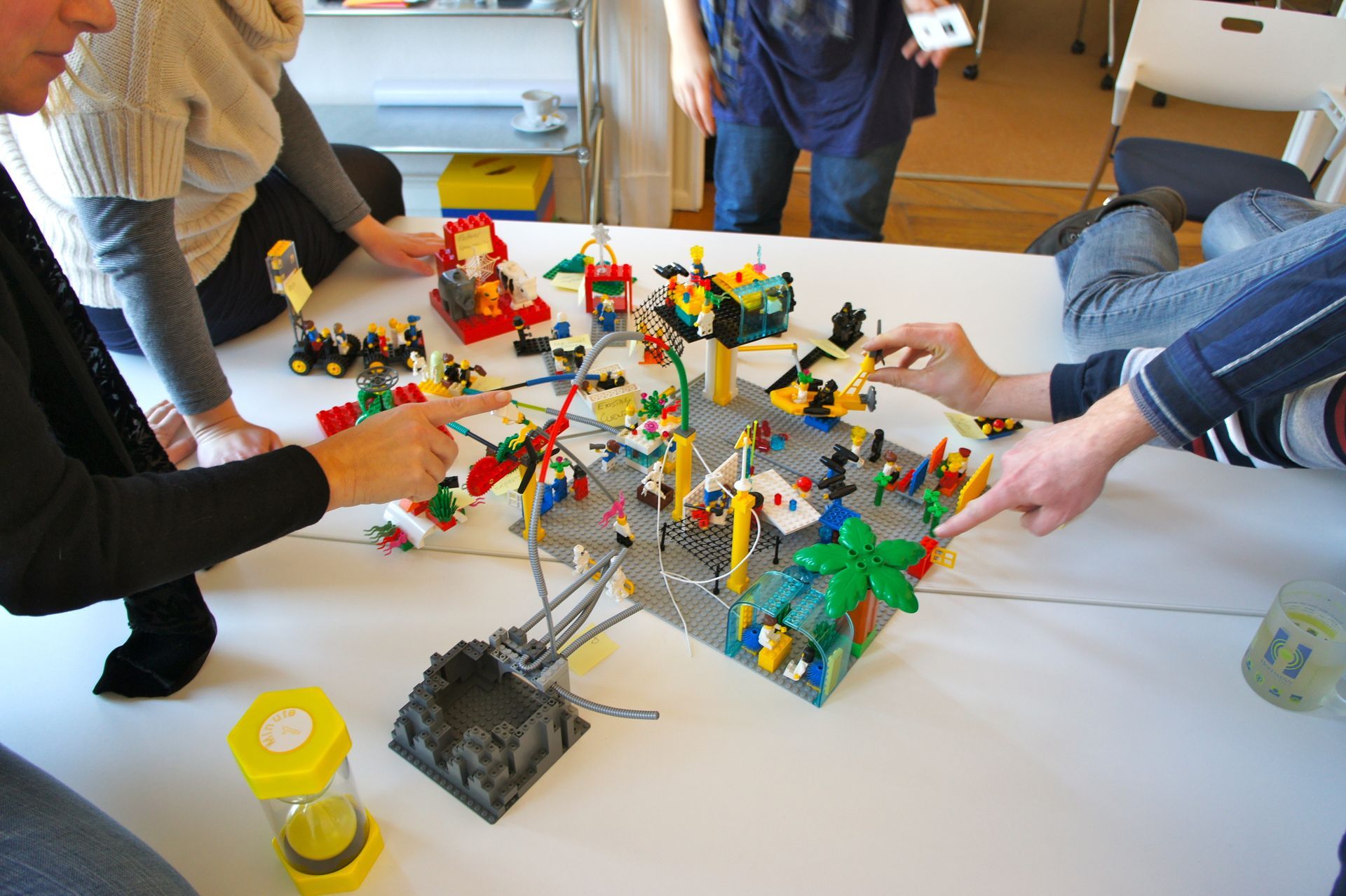 Pessoas brincando com Lego em uma mesa, apontando para as construções.