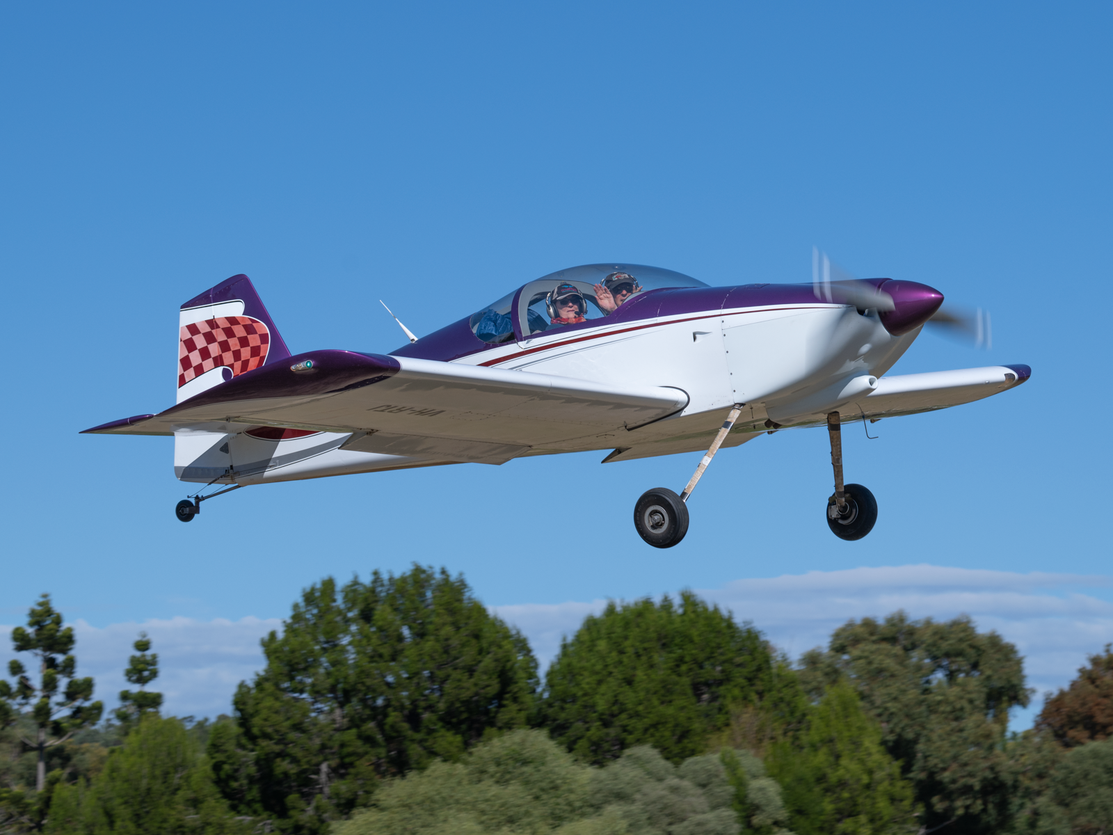 A small purple and white plane is flying in the sky.