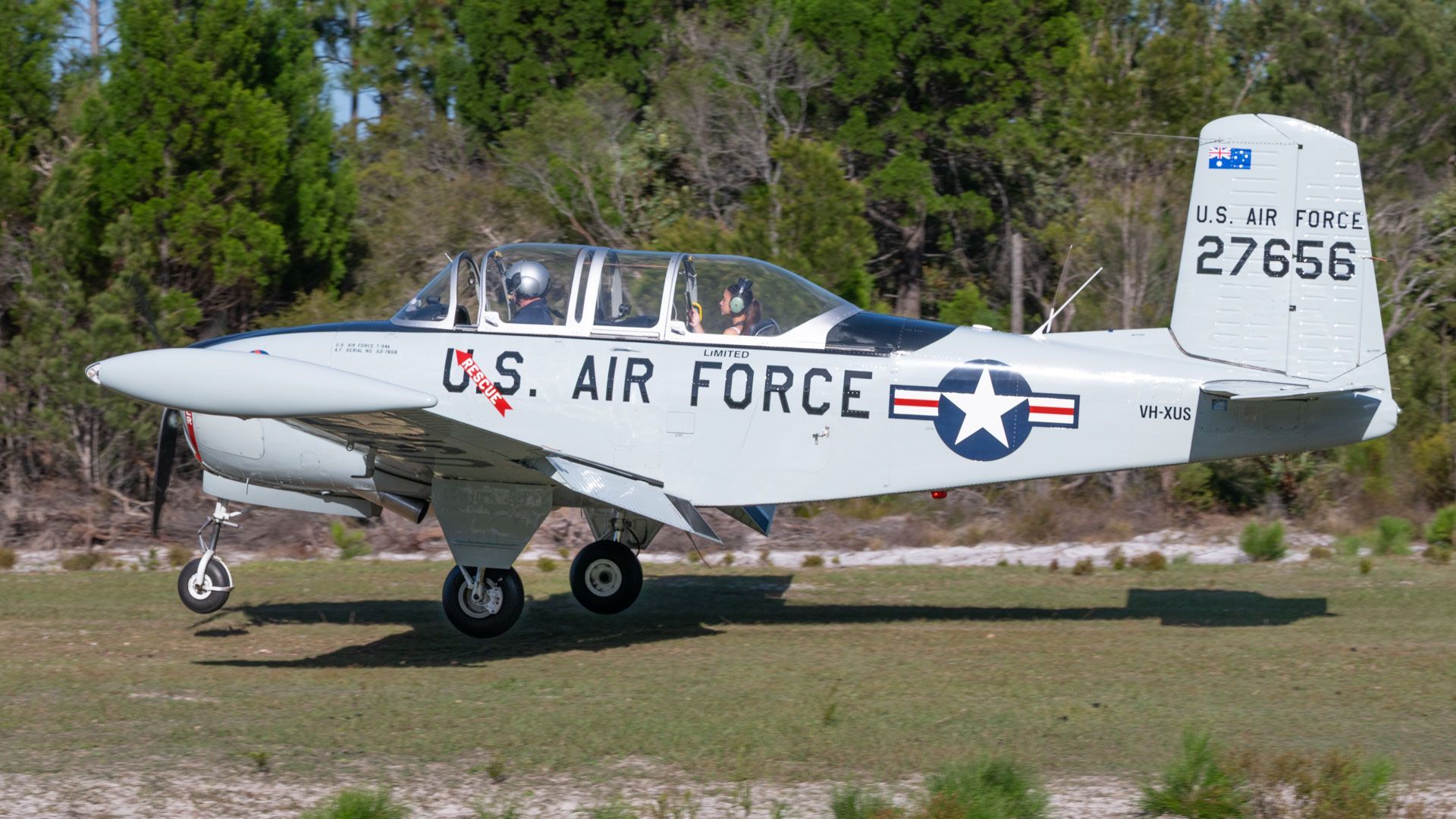White U.S. Air Force trainer aircraft on grass, parked with trees in the background