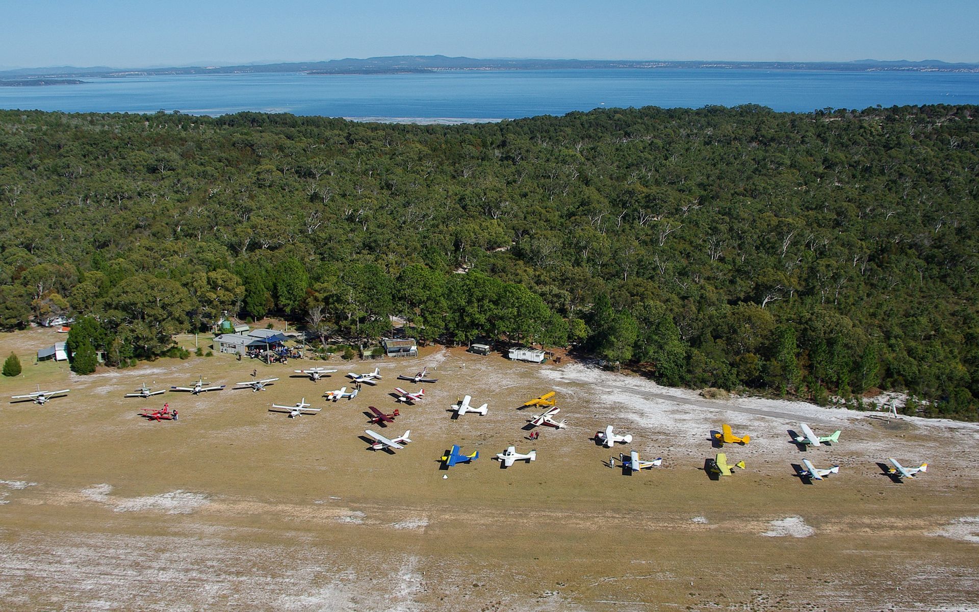 A group of small planes are parked in a field with trees in the background of North Stradbroke island.
