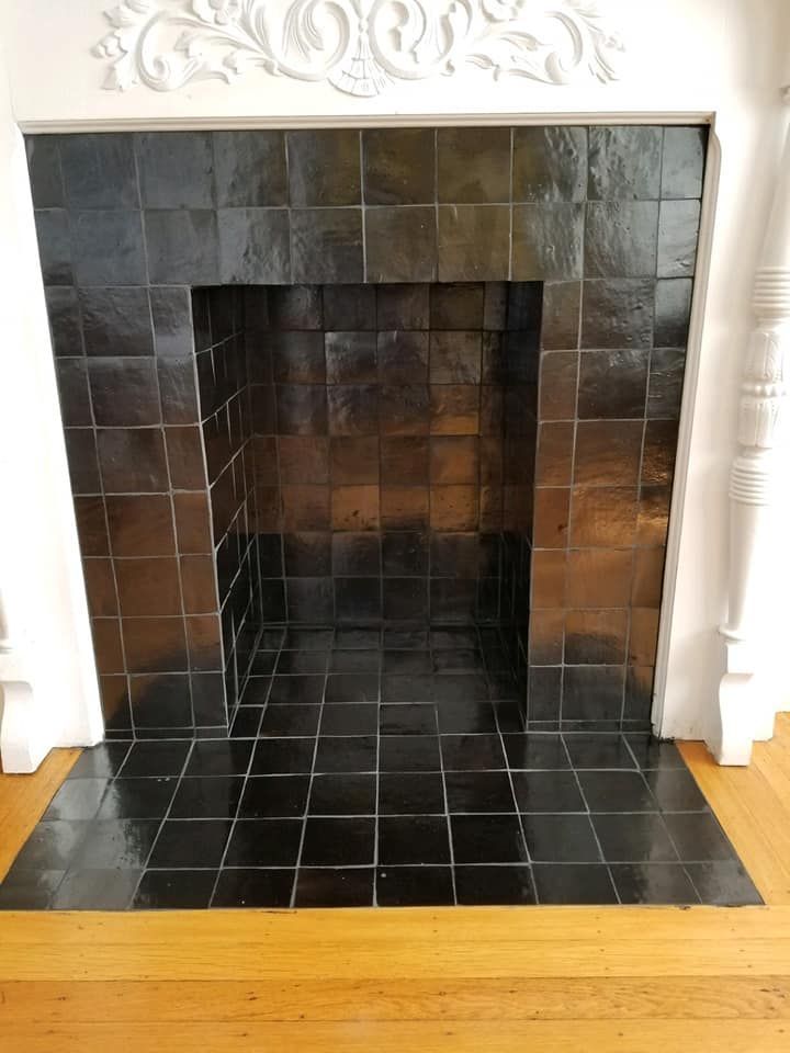 A fireplace with black tiles and a wooden floor in a living room.