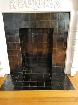 A fireplace with black tiles and a wooden floor in a living room.