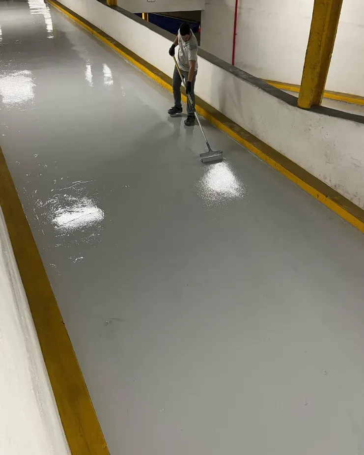 Worker mopping a glossy hallway floor with a wet mop and bucket in an industrial corridor.