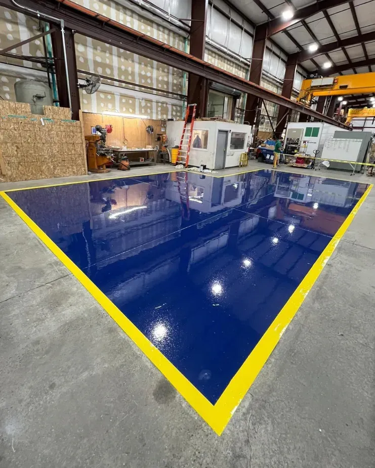 Industrial workshop with a glossy blue floor marked by yellow tape in a warehouse-like space