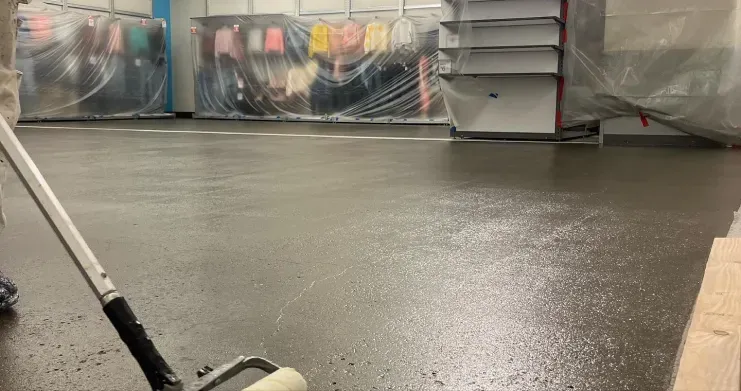 Empty indoor floor area with wet concrete and wrapped equipment along the back wall.