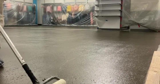 Indoor workshop with a wet black floor, covered equipment, and a mop in the foreground.
