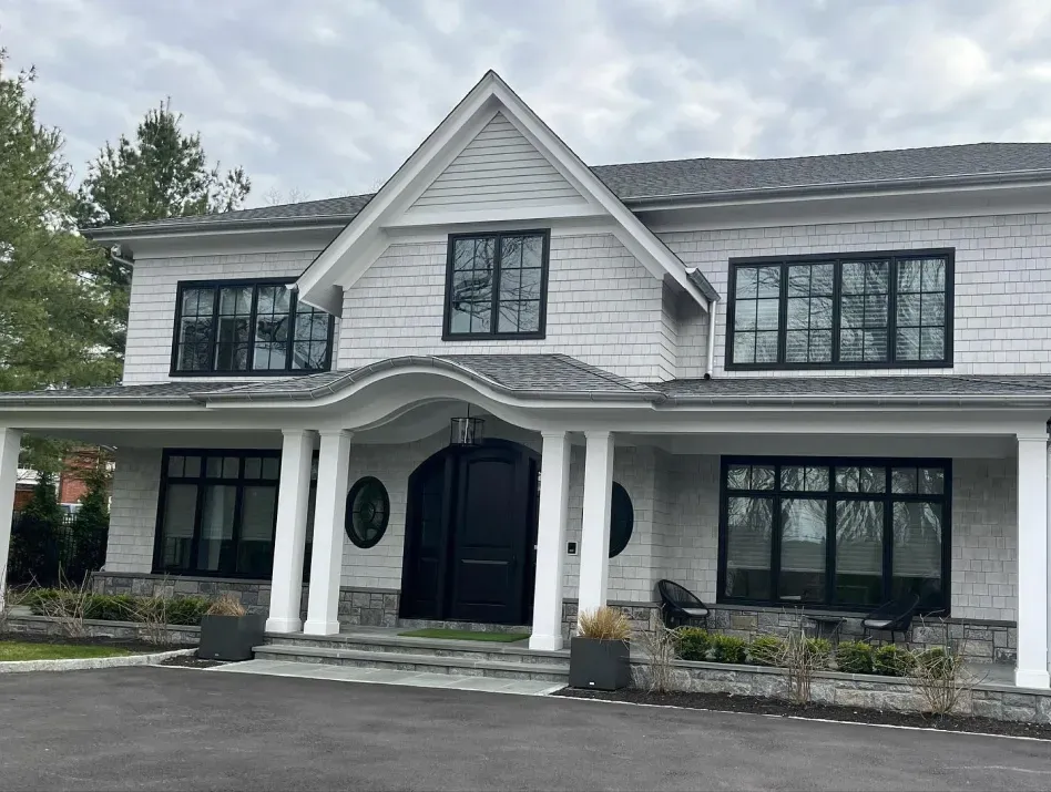 Two-story white house with black trim, arched front porch, and large windows beneath a cloudy sky