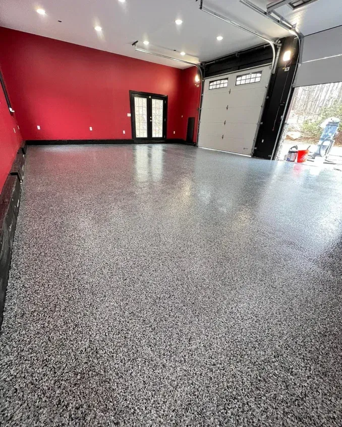 Empty garage with speckled epoxy floor, red and black walls, and open overhead door.