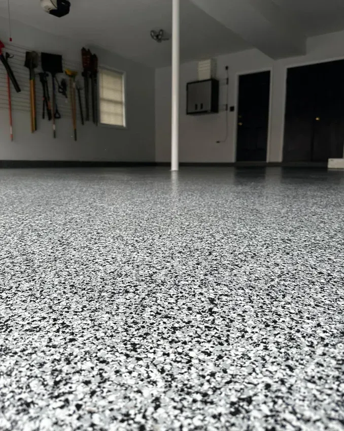 Empty garage with speckled epoxy floor, wall-mounted tools, and a dark open doorway.
