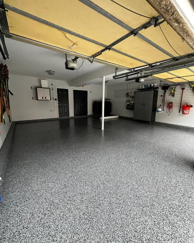 Empty garage with speckled floor, closed yellow overhead door, and storage items on the walls.