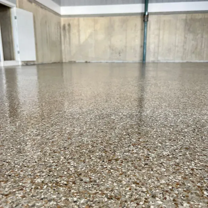 Empty indoor garage with a speckled concrete floor and beige walls.