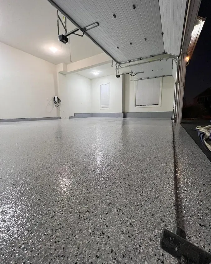 Empty garage with speckled epoxy floor and open overhead door at night.