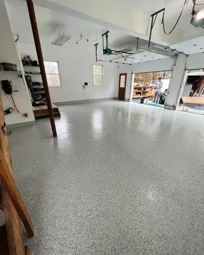 Empty garage with speckled epoxy floor, white walls, and open doorway to storage area