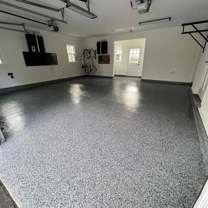 Empty garage with speckled gray epoxy floor, white walls, and closed double doors.