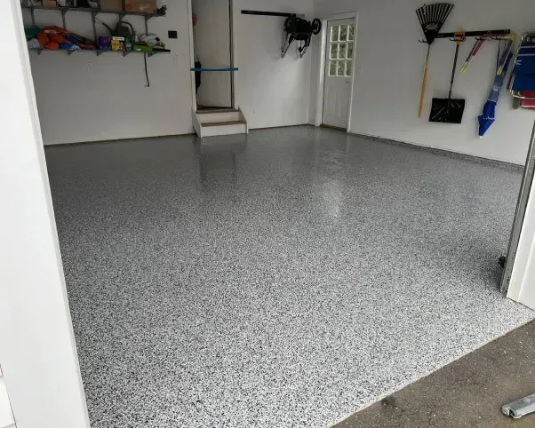 Empty garage with gray speckled epoxy floor and wall-mounted storage shelves.