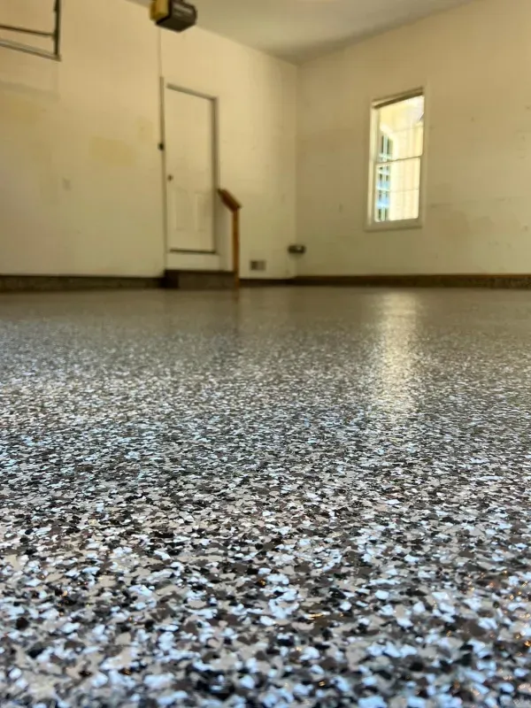 Empty room with speckled epoxy floor, beige walls, and a small window.