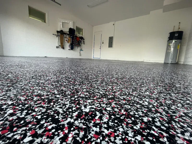 Empty garage with speckled epoxy floor, white walls, wall-mounted tools, and a water heater.
