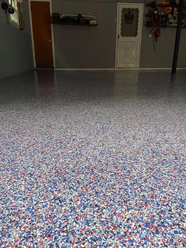 Speckled red, blue, and white epoxy garage floor extending into a dim garage interior.